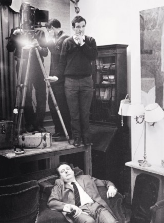 On the set of 'La Peau douce' (1964). Truffaut seems to be asking for silence so that actor Jean Desailly can continue his nap. In fact, Desailly needed all the sleep he could get because after filming during the day he would act in the theatre at night. To keep costs as low as possible, Truffaut filmed the family scenes in his apartment. (c) Raymond Cauchetier