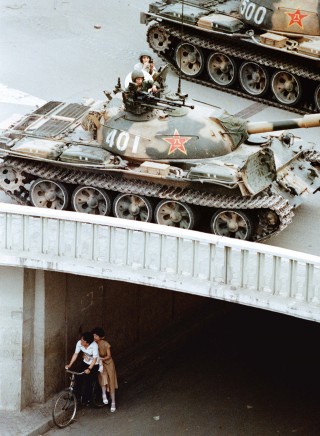 On June 5, 1989, a young couple waits beneath Jianguomenwai Bridge on the fringe of Beijing's diplomatic area, as PLA tanks roll above them. Martial law had been in place since the end of May. Photo (c) Liu Heung Shing, 1989