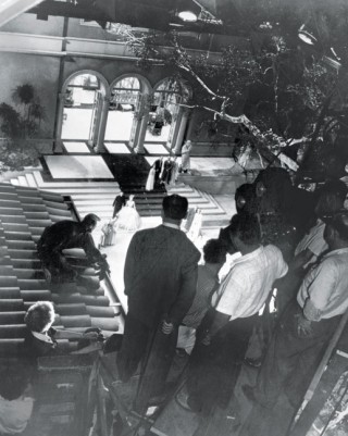 On the set of 'To Catch a Thief' (1955). Hitchcock holds onto a pole in the centre foreground whilst filming the climactic rooftop chase.