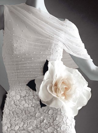 Valentino Garavani. Una grande storia italiana. Haute Couture. Spring-Summer 2004, Mod. 132. Draped point d’esprit evening dress with a slipstyle neckline and a cleverly draped sleeve; the bustier features tight little horizontal pleats, the hips are accentuated by macramé lace, and the skirt is edged with an organza flounce that covers another two underskirts in point d’esprit with rhinestone embroidery; they in turn conceal a third pink organza skirt and a fourth fleshcolored chiffon skirt, all with a flounce trim (detail).